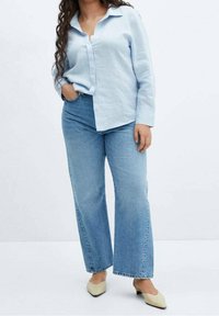 Chemise boutonnée en lin bleu clair associée à des jeans bleus taille haute et à jambes larges. Des mules beiges complètent la tenue.