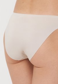 Jasno beżowe bikini o kroju majtek wykonane z gładkiego, elastycznego materiału. Charakteryzuje się niskim stanem oraz minimalistycznym wzornictwem bez widocznych szwów.