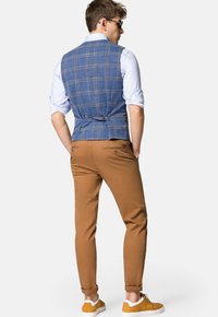 Niebieska kamizelka w kratę z zapięciem z tyłu, zestawiona z wąskimi brązowymi spodniami i żółtymi trampkami. Koszula ma podwinięte rękawy i lekki wzór.