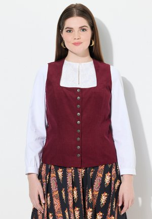 Burgundy corduroy-vestti, jossa on neliön muotoinen kaula-aukko, hopeanväriset napit edessä, yhdistettynä valkoiseen paitaan ja kuviollisiin mustiin hameisiin.