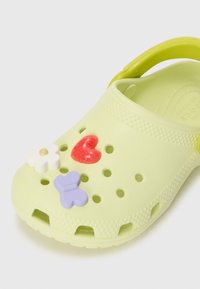 Sabot en caoutchouc vert clair orné de fleurs, de cœurs et de papillons. Comprend des trous de ventilation et une sangle arrière pour un maintien sûr.