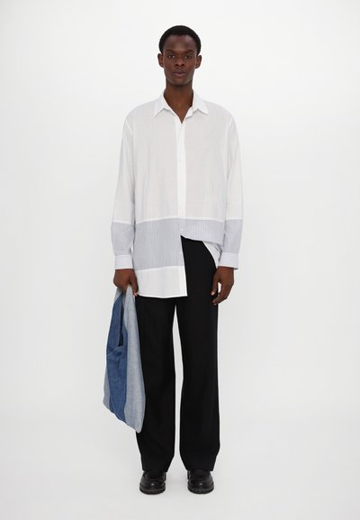 Chemise à rayures blanches et bleues à manches longues avec un col boutonné, assortie à un pantalon large noir et tenant une veste en denim.