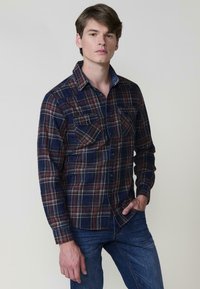 Camicia a maniche lunghe a quadri in navy, rosso e beige; presenta due tasche sul petto e un colletto abbottonato, realizzata in un tessuto testurizzato.