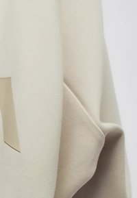 Cream-colored fabric drapes, featuring a smooth texture with a raised beige accent. The material appears soft and lightweight, with subtle folds.