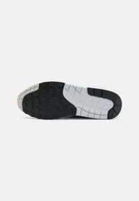 Semelle de sneaker noir et blanc avec un motif de bande de roulement en caoutchouc texturé, avec une rainure grise proéminente et un bord blanc.