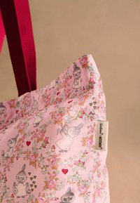 Geantă de umăr roz cu modele florale și personaje din desene animate, având un etichetă și mânere roșii rezistente pentru o transportare ușoară.
