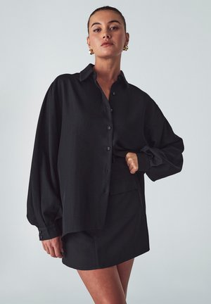 Černá oversized košile s dlouhými rukávy, s límečkem a textured látkou, doplněná o odpovídající černou minisukni.