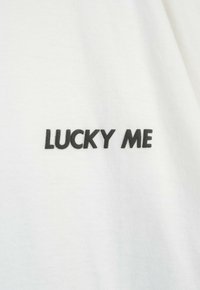 Biała bawełniana koszulka z krótkim rękawem z napisem "LUCKY ME" w odważnym, czarnym tłumaczeniu na klatce piersiowej. Gładka faktura i prosty design.