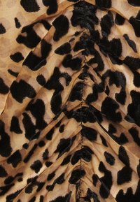 Leopardenmuster-Stoff, der eine Kombination aus hellbraunen und schwarzen Farben zeigt, mit einer strukturierten Oberfläche und gerafften Details.