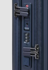 Marineblauer Koffer mit Stofftextur, zwei Reißverschlüssen, einem TSA-Schloss und einem Zahlenkombinationswahlrad. Enthält eine Steckdose und Markendetail.
