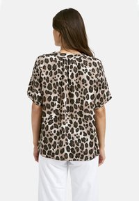 Bluse mit Leopardenmuster aus leichtem Stoff, mit kurzen Ärmeln, einer Rückenfalte und einem runden Ausschnitt. Erdtöne dominieren das Design.