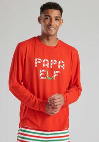 Camisa roja de manga larga con el texto "PAPA ELF" en letras estilo bastón de caramelo. Presenta un corte relajado y una tela suave y lisa.