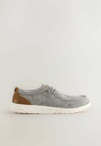 Chaussure décontractée en tissu gris avec un patch au talon marron et une semelle blanche mouchetée, dotée d'une fermeture à lacets et d'un design profilé bas.