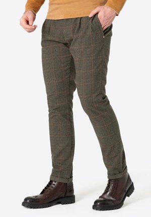 Green patterned trousers with orange check, textured fabric, and side pockets. Paired with dark brown boots featuring brogue detailing.