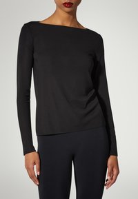 Svart långärmad topp med båthals och mjuk tyg; figurnära design med lätt drapering vid midjan. I kombination med svarta leggings.