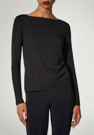 Zwarte lange mouwen top met een bootvormige halslijn en een gladde stof; aangesloten ontwerp met lichte draping bij de taille. Gecombineerd met zwarte leggings.