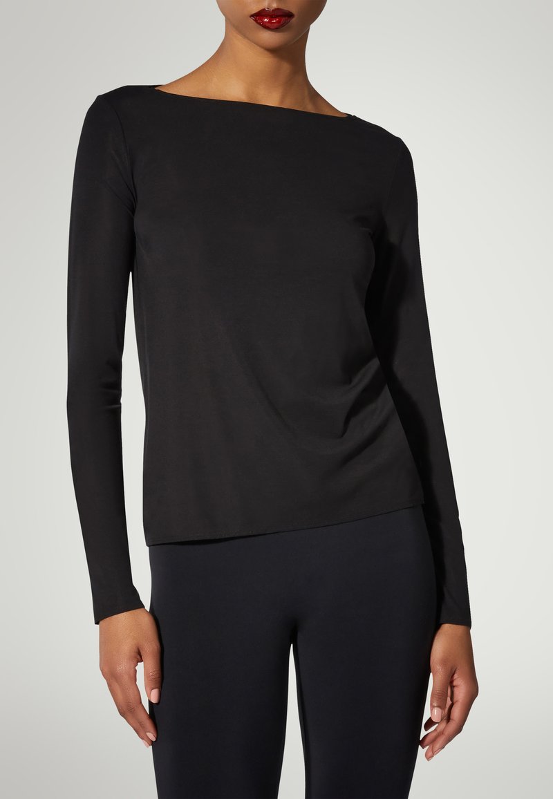 Svart långärmad topp med båthals och mjuk tyg; figurnära design med lätt drapering vid midjan. I kombination med svarta leggings.