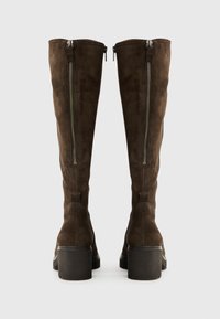 Bruine suede laarzen tot de knie met een chunky zool en zijritsen. De textuur is glad, met een gestroomlijnd ontwerp en scherpe lijnen.