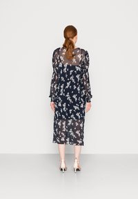 Vestido floral azul marinho feito de tecido translúcido, com mangas bufantes longas, comprimento médio, e um design em camadas que revela um vestido interior sólido.