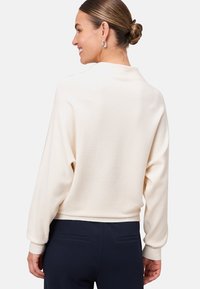 Pull crème côtelé avec une coupe décontractée, des épaules tombantes et des manches à poignets, associé à un pantalon marine. Design simple, sans motifs visibles.