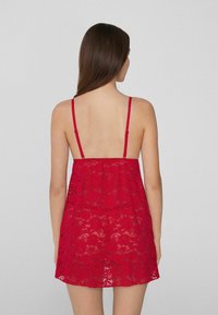 Bralette de encaje rojo con tirantes finos, de ajuste holgado y textura transparente, que muestra patrones florales en toda la tela.