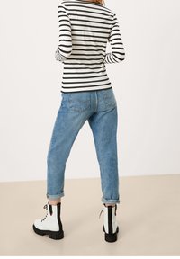 Pasekowana czarno-biała bluzka z długim rękawem, jasnoniebieskie jeansy o luźnym kroju oraz białe botki na kostkę z czarnymi akcentami. Widoczne przeszycia i podwinięte mankiety.