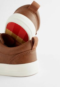 Brune sneakers med overdækning af syntetisk læder, rund tå, hvid gummisål og tekstureret rød og gul indersål. Inkluderer en trækflig ved hælen.