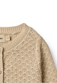 Gilet en tricot beige présentant une texture ouverte et aérée, un col côtelé et une fermeture à boutons. Tissu léger et respirant, idéal pour le superposé.