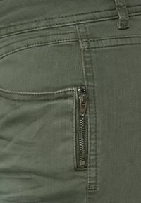 Oliwkowe dżinsowe spodnie z zamkiem błyskawicznym na boku, z widocznym szwem i gładką teksturą.