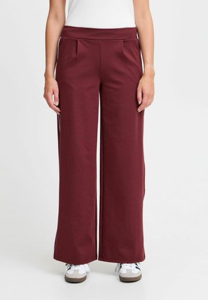 Burgundy wide-leg pants with a smooth texture, featuring a high waistband and front pleats. Worn with white sneakers against a plain background.