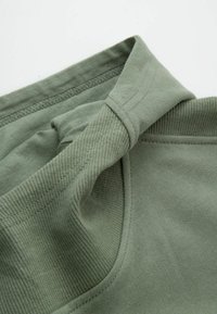 Jasnooliwkowy bawełniany produkt o miękkiej teksturze, z prążkowanym kołnierzem i gładkim materiałem. Szczegółowe szwy i złożone krawędzie tkaniny.