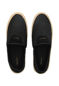 Zapatos negros de tela trenzada tipo slip-on con suela de yute de espadrille. Presentan un tejido texturizado, bordes elásticos y una marca dorada en la plantilla.
