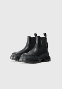 Zwarte leren enkelboots met elastische zijkanten, trekflappen en een robuuste rubberen zool met uitgesproken profielpatronen.