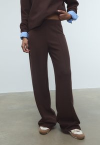 Ruskeat, leveälahkeiset housut sauman yksityiskohdilla, yhdistettynä tummanruskeaan yläosaan ja vaaleansinihin paidankauluksiin, käytetään valkoisten ja ruskeiden lenkkareiden kanssa.