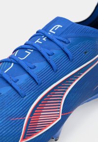Blaue Sportschuhe mit detaillierter Textur, blauen Schnürsenkeln und einem rot-weißen gestreiften Logo an der Seite.