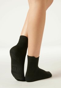 Svarta ankelsockor med ribbat mönster och greppprickar på sulorna. Tyget är mjukt med en elastisk passform, designat för komfort och stabilitet.