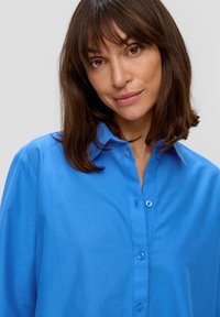 Camicia azzurra con colletto, caratterizzata da maniche lunghe e una trama liscia. I dettagli notevoli includono bottoni azzurri chiari.