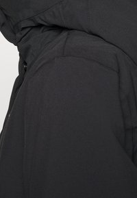 Chaqueta con capucha negra con textura suave, costuras cosidas y vista en primer plano del detalle del área del hombro y el cuello.