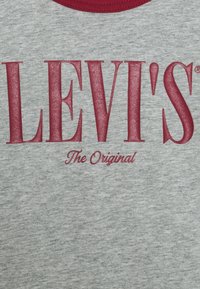 Szara bawełniana koszulka z okrągłym dekoltem. Wyróżnia się odważnym czerwonym logo "LEVI'S" oraz mniejszym tekstem poniżej: "The Original" w jaśniejszym odcieniu czerwieni.