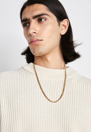 Kuldne kettkaelakee, mis on kantud kreemjas ribakudumisest ülesse; pehme tekstuur kõrgema kaelusega ja õrn muster kangas.