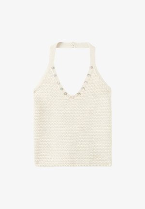 Giovane donna in piedi contro un muro beige che indossa un top lavorato a maglia bianco, pantaloncini grigio chiaro e sandali marroni con borchie.