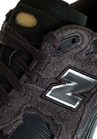 Sneaker in suede nero con finitura viola testurizzata, logo grigio prominente e dettagli in mesh. Lacci e parti metalliche sono nere.