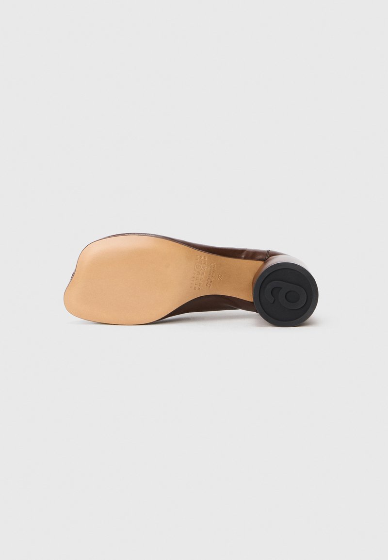 Scarpa in pelle marrone vista dal lato della suola che mostra la suola in pelle beige e il tacco rotondo nero con logo in rilievo.