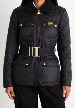 Black quilted jacket with gold buttons and zipper, belted waist, four front pockets, and a textured collar on a person from neck to hips.