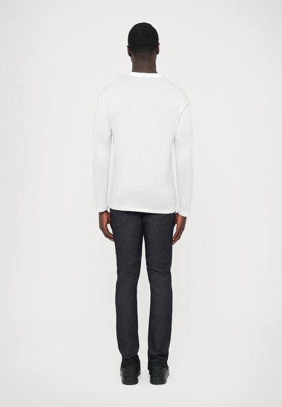 Λευκό μακρυμάνικο πουκάμισο με στρογγυλή λαιμόκοψη σε συνδυασμό με σκούρο τζιν. Η πίσω όψη δείχνει εφαρμοστή γραμμή με λεία υφή υφάσματος.