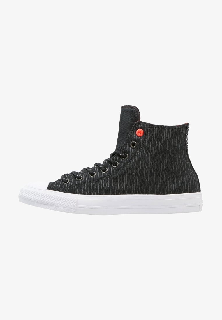 Baskets montantes noires avec semelle et embout en caoutchouc blanc, lacets noirs, motif vertical subtil et petit œillet rouge près de la cheville.
