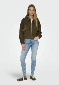 Maslinasto zelena kaširana bomber jakna s kapuljačom, zatvaranjem na zip i dva prednja džepa. Nosena s svijetlop Plavim uskim trapericama i cipelama s uzorkom leoparda.