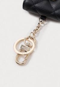 Čierna prešívaná kožená taška s veľkým zlatým kovovým reťazcom a krúžkovým zapínaním, ktoré obsahuje detail zámku, prešitou textúrou a hladkými akcentmi.