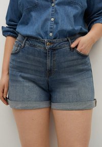 Pantalones cortos de mezclilla en azul oscuro con dobladillo enrollado, que cuentan con cinco bolsillos, cierre de botón y un diseño clásico de corte recto.