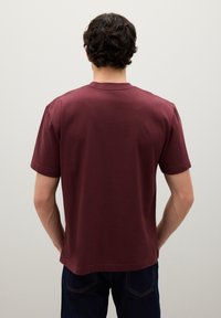 Camiseta corta de algodón en color burdeos, con cuello redondo y corte relajado. La parte trasera es sencilla con costuras visibles y una textura suave.